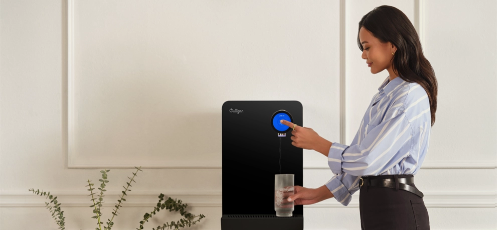 Frau bedient einen Culligan Wasserspender im Büro und hält ein Glas Wasser in der Hand